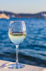 A glass of white wine with a reflection of the coast in it. Relax at a table in a restaurant by sea