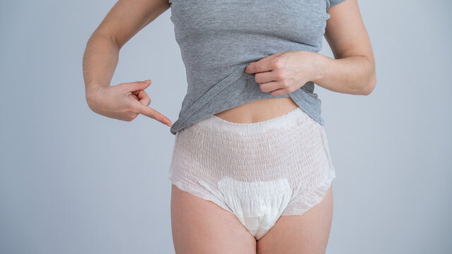 A cropped portrait of a woman pointing at adult diapers on her. Urinary incontinence problem. 