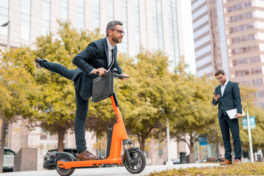 Funny excited business man on electric scooter on city street. Employee business man corporate lawyer in suit riding electric e scooter. Crazy business, fast and easy.
