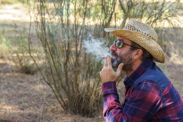 man with beard and hat smoking a cigarette in the forest, fire hazard concept