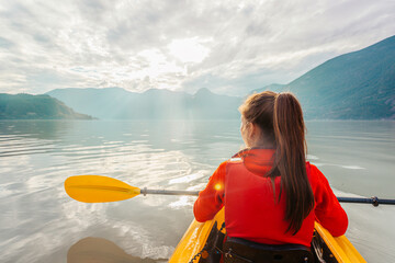Woman kayaking paddling in kayak in fjord surrounded by mountains. People living healthy active...