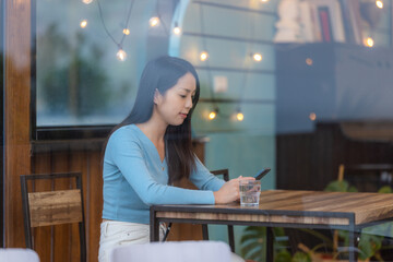 Woman look at mobile phone and sit inside the coffee shop