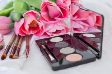 Obraz na płótnie Canvas Pink tulips, eye shadow palette with mirror, brushes on white background, women makeup cosmetics set