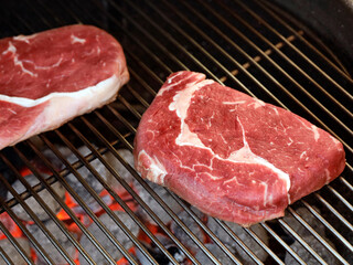 Raw Rib Eye Steak on grill grate over charcoal grill, preparing beef steaks on barbecue