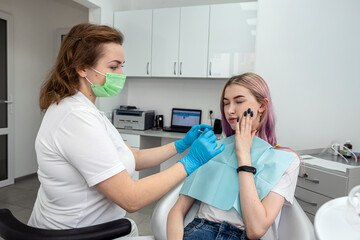 patient sitting dental chair next to female dentist doctor who is conducting an examination.