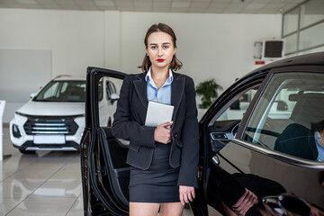 alone pretty car saleswoman in suit holding clipboard in new car showroom