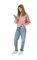 Full length portrait of cute girl in pink sweater and blue jeans standing and chatting on the cell phone, isolated on white background. Cute teenager with hand in pocket smiling and posing in studio.