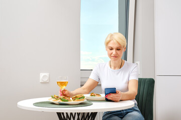Obraz na płótnie Canvas Senior woman reading news from smartphone while having breakfast
