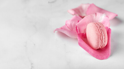 Gentle pink macaron placed on rose petals. Light grey marble background, copy space to insert text or design. Valentin's Day, Mother's Day, romantic occasion concept.