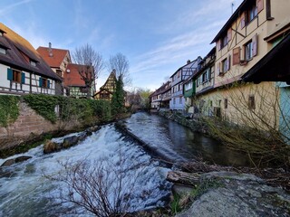 Fototapeta na wymiar Medieval stone bridge over river in centre of Kaysersberg, small town in Alsace (France, Europe) in wintertime