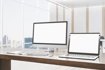 Modern designer office desktop with empty white mock up computer screens, supplies and blurry interior with windows and city view background. 3D Rendering.