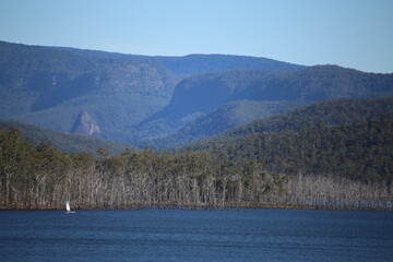 Sailing Boat on Blue Lake with Mountains and Green Trees in the background Centred Left of Frame