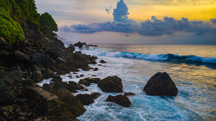 sunset over the sea and waves hits rocky beach in Lombok Island, Indonesia
