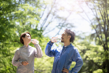 Two middle couples drinking water in a park with fresh greenery, running in sportswear, etc.