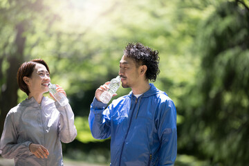 新緑の公園で水を飲むミドル夫婦2人　スポーツウェアでランニングなど © kapinon