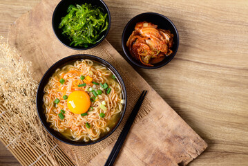 Asian instant noodle soup with fresh egg yolk eating with kimchi cabbage and seaweed salad, Table...