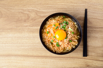 Asian instant noodle soup with fresh egg yolk on wooden background, Table top view