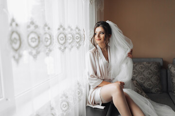 Portrait of the bride. A brunette bride is sitting on a gray sofa in a dressing gown, posing,...