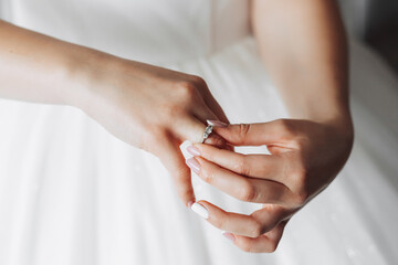 A brunette bride in a white dress puts on her silver wedding ring. French manicure. Open shoulders. Beautiful hands. Long veil. Morning of the bride. Details