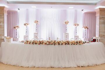 The wedding table of the bride and groom, decorated with flowers, white tulle, made in light pink color. Flowers on stands. Wedding details. Light