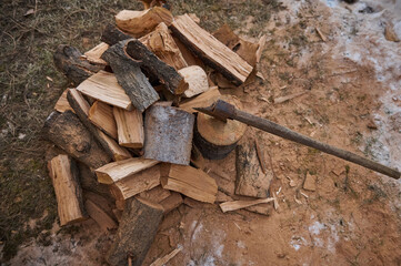 Still life. View from above of a heap of wood for making fire. Partial view of an ax or hatchet in a stump near firewood in rustic background. Renewable energy. Preparation for cold winter. Close-up