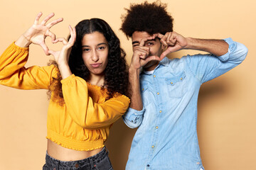 Studio portrait of cool couple making faces and showing love gesture. Young latin girl having fun...