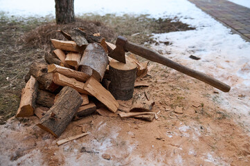 Chopping log with an old ax with a wooden handle for making a fire in a snowy forest. Picnic and outdoor recreation. Rustic still life with hatchet in stump near firewood against the nature background