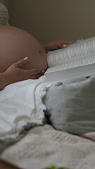 A pregnant woman is reading a book in bed.