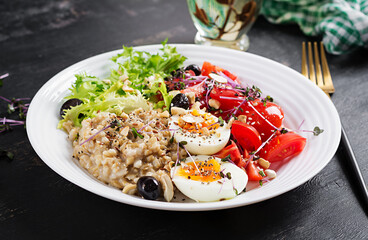 Breakfast oatmeal porridge with boiled egg, cherry tomatoes, olives, nuts and microgreens. Healthy balanced food.