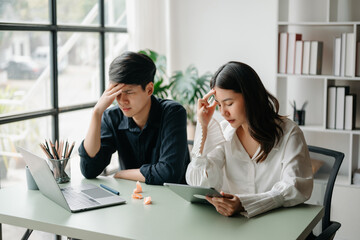 Fototapeta premium Two Asian people feeling migraine head strain.Overworked businesswoman financier while working on laptop and tablet at home office.
