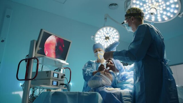 Young surgeon and nurse perform plastic surgery procedure on face looking at medical monitor. Modern equipment, high-quality lighting in the background. High quality 4k footage Generative AI