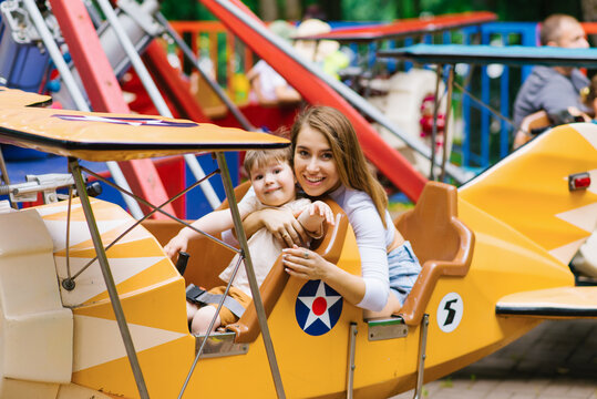 Young mom and her little son's family weekend at an amusement park. A mother and her boy ride bright fun rides