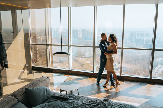 Young adult caucasian couple embracing at contemporary apartment in skyscraper  enjoying vacation on summer. Newlyweds traveling. Bearded young caucasian man hugs girlfriend home. - Powered by Adobe