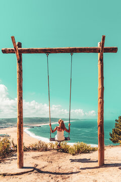 Woman swinging on swing enjoying beautiful ocean panoramic view- Portugal
