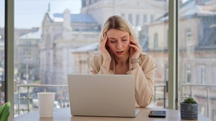 Busy ill woman in jacket sitting at cafe or office table near window with city background working on laptop feeling strong headache massages the temples. Overwork, pain and human lifestyles concept.