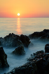 Long time exposure of the sunset at the sea with rocks in the foreground