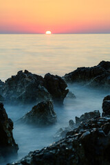 Long time exposure of the sunset at the sea with rocks in the foreground