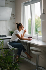 Young woman nutritionist blogger conducts a consultation or an open lesson by video link telling about the benefits of fresh berries, sitting in the kitchen with a plate of cherries