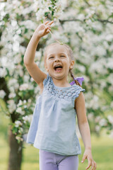 Girl has fun in the blooming garden in the spring outdoors and laughs loudly