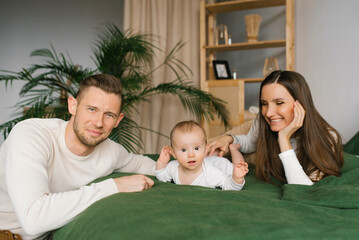 Mother and father are lying on the bed with their little son at home