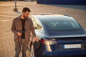 Back view of the automobile. Man is standing near his electric car outdoors