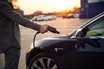 Putting charger into socket. Man is standing near his electric car outdoors