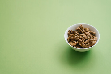 Peeled walnuts on a white plate on a green background with copy space