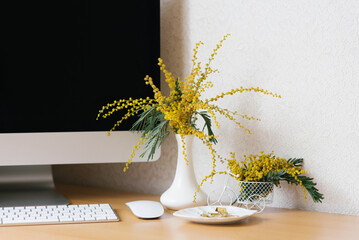 Concept of a business, freelancer, blogger. The laptop is on a wooden table against a white wall with a mimosa in a vase