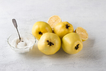 Fresh quince, lemon and a bowl of sugar for a delicious vegan dessert on a light gray background
