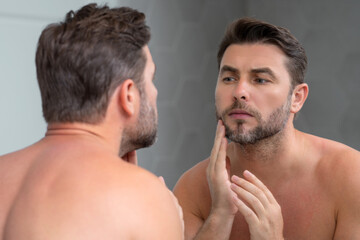 Naklejka premium Close-up portrait of perfect brunet man touching chin and skin. Handsome man touching face in front of the mirror in bath. Perfect skin. Man cosmetic, skin treatment. Hygiene and skin care male face.