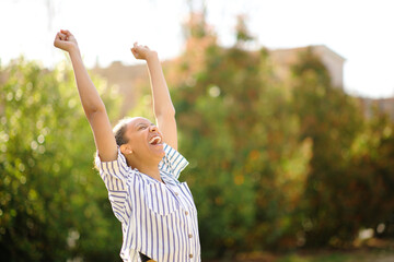 Excited black woman raising arms in a park