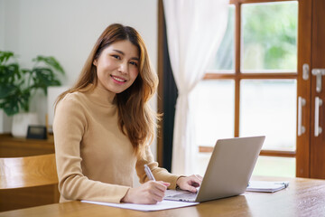 Happy beautiful Asian woman using computer laptop for work online at living room.