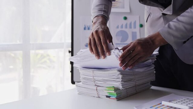 work from office A businessman works a bunch of paper files to find information on his desk at home. business report pile of unfinished documents