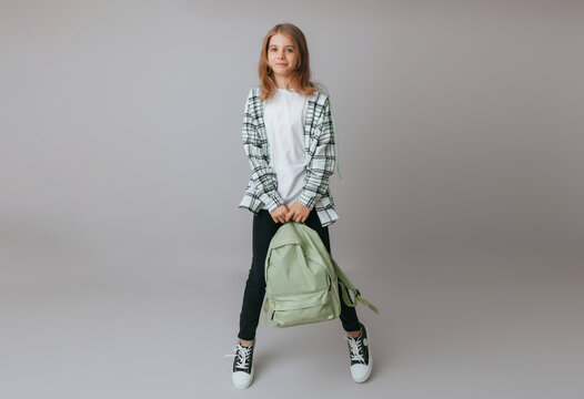 cheerful teenage girl 11,12,13 years old in a school uniform wears a backpack on a gray background. school fashion